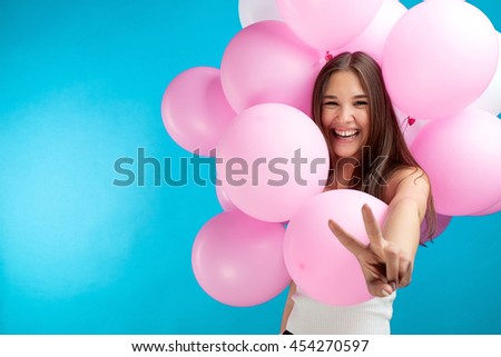 Portrait of laughing candid girl with pink air balloons with peace sign on blue background