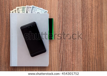 The daily log with denomination hundred, fifty, twenty, and ten dollars and a credit card on a wooden table with black business smartphone.