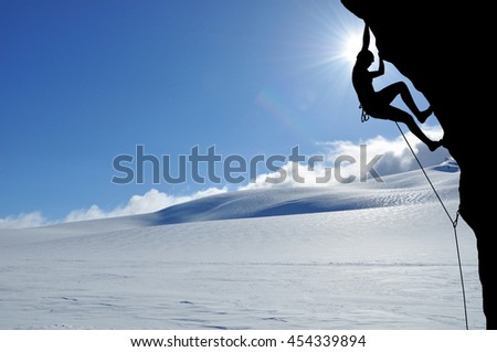 Silhouette of young woman lead climbing on overhanging cliff high above clouds and mountains, sun, beautiful colorful sky and clouds behind. Climber on top rope, hanging on rock.