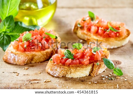 Tasty savory tomato Italian appetizers, or bruschetta, on slices of toasted baguette garnished with basil, close up on a wooden board Royalty-Free Stock Photo #454361815