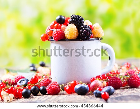 various fresh berries on wooden table, over green background