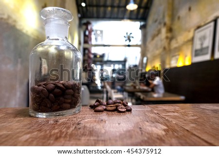 vintage picture tone Roasted brown coffee beans and A small glass jar on a wooden table with coffee cafe shop background