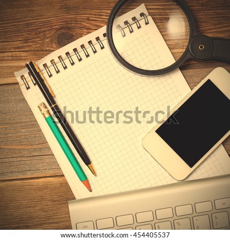 smartphone, computer keyboard, notebook, pen and magnifying glass on old wooden table surface. Still-life with objects for finding and recording information in web. instagram image filter retro style