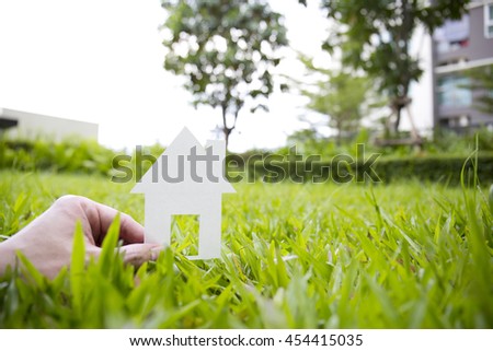 Hand holding house against green field