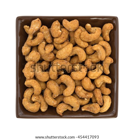 Whole honey roasted cashews in a square brown dish isolated on a white background.