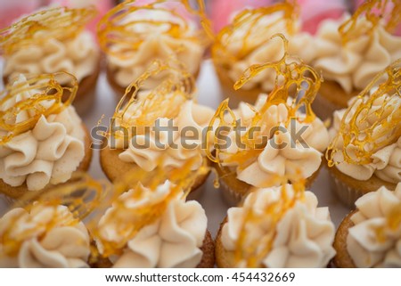 Rows of brightly colored frosted cupcakes of toffee butterscotch flavor with a spun sugar decoration Royalty-Free Stock Photo #454432669