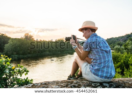 Hiking woman use smart phone making photo of beautiful river nature landscape. Traveler girl sitting on cliff edge, taking picture on mobile phone. Tourist with camera in mountains outdoor on sunset.