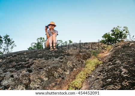 Hiking woman use smart phone making photo of beautiful nature landscape. Traveler girl sitting on cliff edge, taking picture on cellphone. Tourist photographer woman with camera in mountains outdoor.