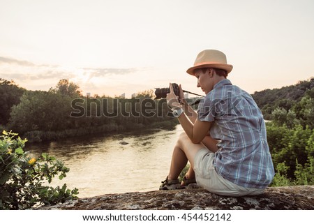 Hiking woman use smart phone making photo of beautiful river nature landscape. Traveler girl sitting on cliff edge, taking picture on mobile phone. Tourist with camera in mountains outdoor on sunset.