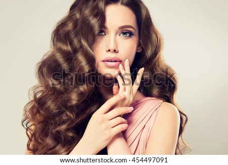 Brunette  girl with long  , shiny wavy hair .  Beautiful  model with curly hairstyle . Woman with beautiful hands  french manicure 