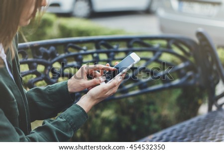 Hipster texting message on smartphone or technology, mock up of blank screen. Tourist girl using cellphone on forged steel bench background. Female hands holding device. Mockup copy space for text