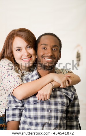 Interracial charming couple wearing casual clothes posing embracing friendly and smiling, white studio background