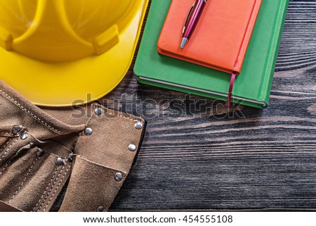 Leather building belt notepads pen protective hard hat on wooden board construction concept.