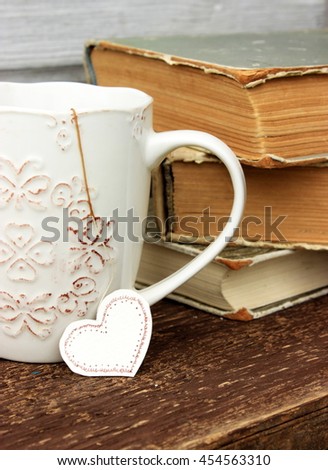 Romantic composition with stack of vintage books with very old paper and covers and cup of hot tasty tea in ceramic cup with label in heart shape.