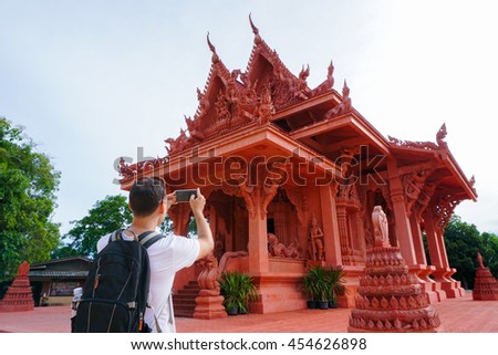 Young male traveler taking photo of Asian buddhist temple. Mobile technologies in tourism