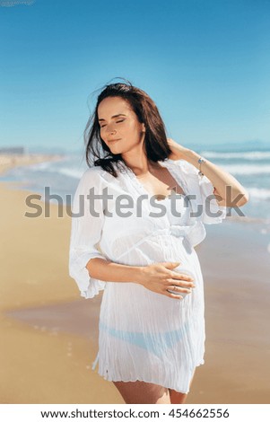 Pregnant wearing a tunic seashore walk. Expectant mother in a beautiful white dress enjoying a sea holiday. Future motherhood.