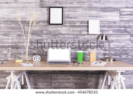 Creative designer tabletop with blank white laptop, clock, coffee and other items with picture frames hanging above on wooden wall. Mock up