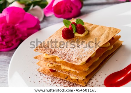 Pastry with raspberries on plate. Pink flowers and mint leaves. Millefeuille with decoration. Crispy dough and juicy berries.