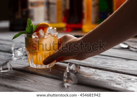 Orange beverage with ice. Hand with glass of cocktail. Your drink is ready. Bartender's original recipe.
