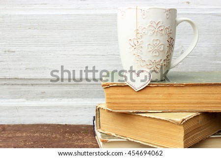Romantic composition with stack of vintage books with very old paper and covers and cup of hot tasty tea in ceramic cup with label in heart shape. Copy space