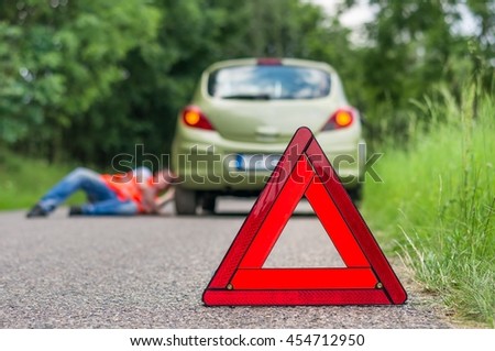 Driver lying under the broken car and warning triangle