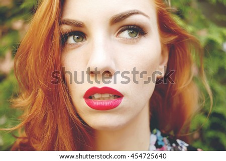 Closeup of beautiful red haired woman with matt red lips and eye makeup, eyeliner. Photo toned style instagram filters