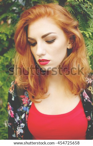 Closeup of beautiful red haired woman with matt red lips and eye makeup, eyeliner. Photo toned style instagram filters