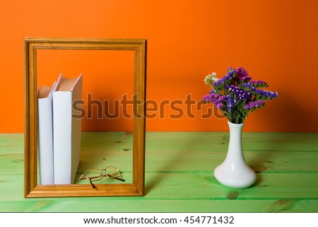 Stack of White books in brown wooden frame on an orange background on a green wooden table, pen, free copy space, vase with Flowers, no labels, blank spine. Back to school