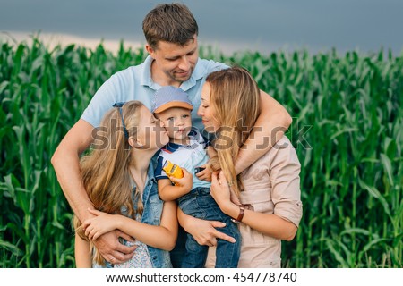 Man hugging his wife, daughter and little son.Cute happy family in front of cornfield and thunder sky. Sister kissing her brother