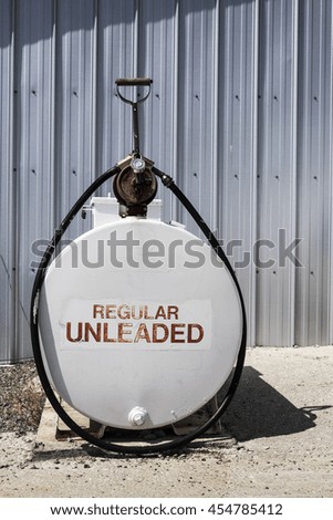 Regular unleaded written in red on a white tank with a black hose wrapped around it.