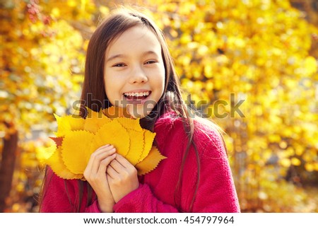 closeup portrait of a beautiful smiling teenage girl with yellow leaves in autumn