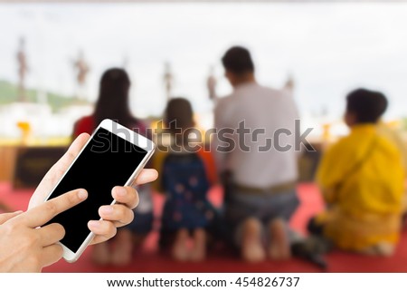 woman use mobile phone and blurred image of people pay respect to kings of thailand monument