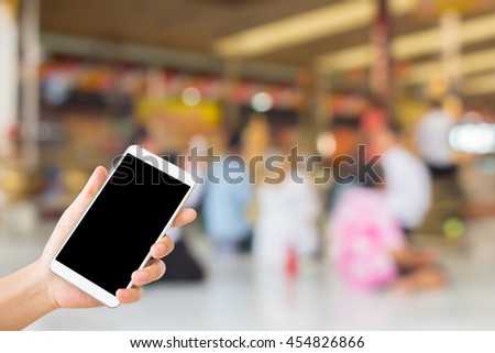 woman use mobile phone and blurred image of buddhist pay respect to buddha image in the temple
