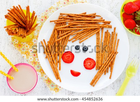 Edible picture on the plate - funny girl face of berries and cookie straws for breakfast for children. Idea for a positive food