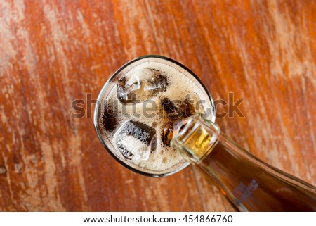 Pouring cola into the glass on old wooden table.
