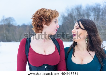 Two beautiful women in fashionable dresses posing in winter forest 