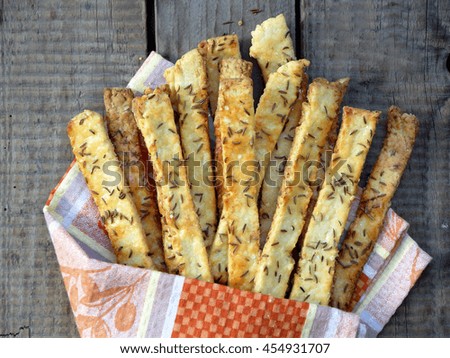 Crispy bread sticks of puff pastry sprinkled with salt and caraway seeds on wooden background.