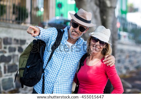 Smiling man pointing while standing with woman on sidewalk in city