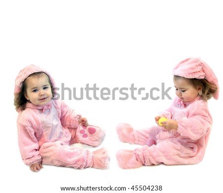 Twin Baby girls dressed in pink bunny costumes are playing with a yellow Easter egg.  One is looking and the other is holding the egg.