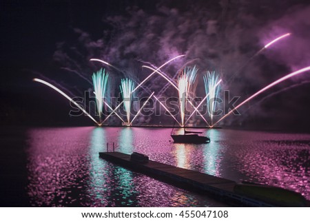 Ignis Brunensis violet purple and green colored fireworks resembling aster flower reflecting on dam water surface. Long exposure night graphical photography using creative tilt effect tilt-shift lens.