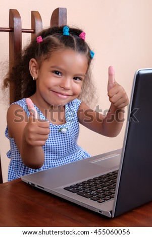 Multiracial small girl using a laptop computer and doing the thumbs up sign