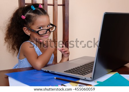 Funny multiracial small girl wearing glasses and using a laptop computer at home