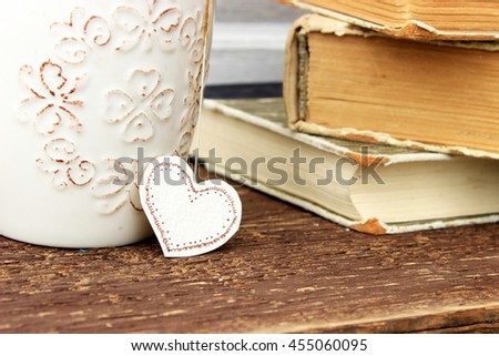 Romantic composition with stack of vintage books with very old paper and covers and cup of hot tasty tea in ceramic cup with label in heart shape. 