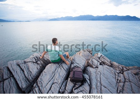 A tourist with a backpack sitting on the rock and looking at the sea