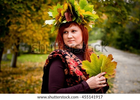 The girl with red hair in the woods. Golden colorful fall. Beautiful bright happy woman with wreath of maple leaves on the head.