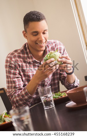 Picture of smiling man sitting at table in vegan restaurant or cafe. Happy man looking at his vegan burger. Healthy and delicious food concepts.