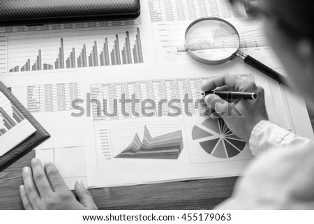 Girl and business accessories (notebook, calculator, planchette, tablet, fountain pen, glasses) and graphics, tables, charts on white sheets on office desk. Soft focus. Black and white.