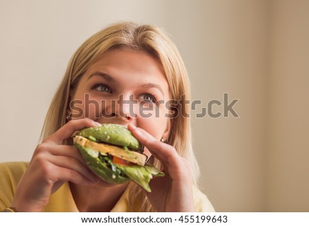 Image of beautiful woman eating vegan burger in vegan restaurant or cafe. Closeup picture of hungry lady eating healthy food. Vegan concept.