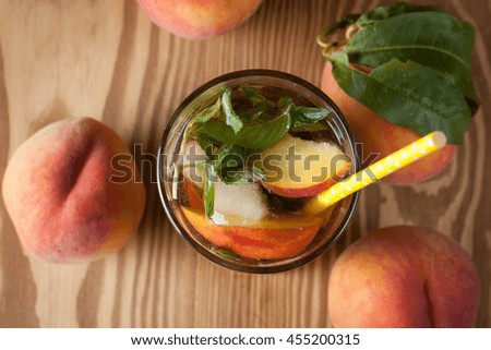 Fresh, cold peach tea with mint, ice cubes and peaches fruits on wooden background.
