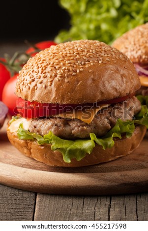 Close-up photo of home made hamburger of beef, onion, tomato, lettuce, cheese and spices with a glass of light beer. Fresh burger closeup on wooden rustic table with potato fries and chips.